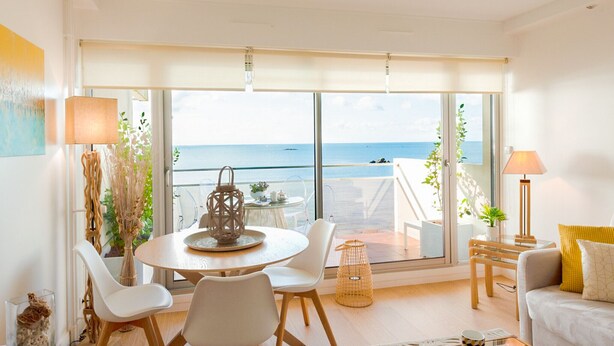 Un salón moderno con un amplio ventanal con vistas al mar, una mesa de comedor redonda y una zona de estar acogedora.