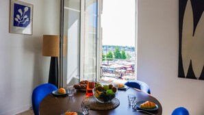Un coin repas avec une table dressée pour deux personnes, un saladier de fruits, des croissants et un verre d’eau.