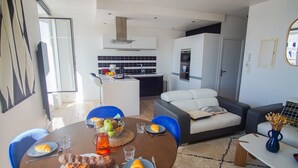 Un salon moderne avec un coin repas, comprenant un canapé, une table basse et une cuisine en arrière-plan.