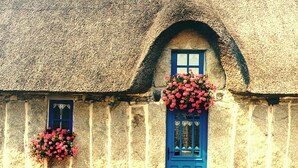 A traditional stone building with a thatched roof, a blue door, and flower baskets. - -Mave Maï- Magnifique T3 surplombant la mer (Concarneau)