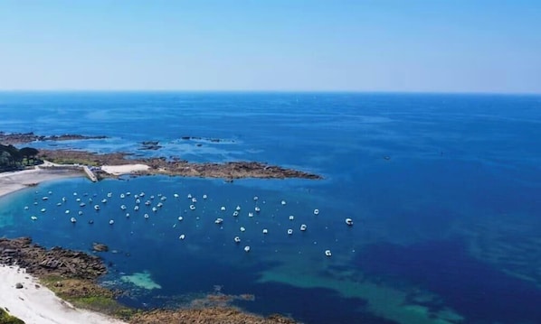 Luchtbeeld van een kustgebied met helderblauw water, rotsformaties en tal van boten in een baai afgemeerd.