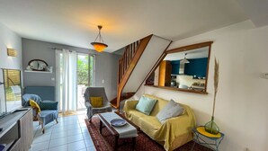Un salon comprenant un canapé, un fauteuil et une table à manger. Un escalier mène à l’étage supérieur.