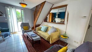 Un salon comprenant un canapé, une table basse, un fauteuil, un escalier et une grande fenêtre.