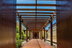 A covered walkway with a wooden floor and metal railings, leading to a circular opening. - Villa Cantik Pandawa By Fays Hospitality (Bali)