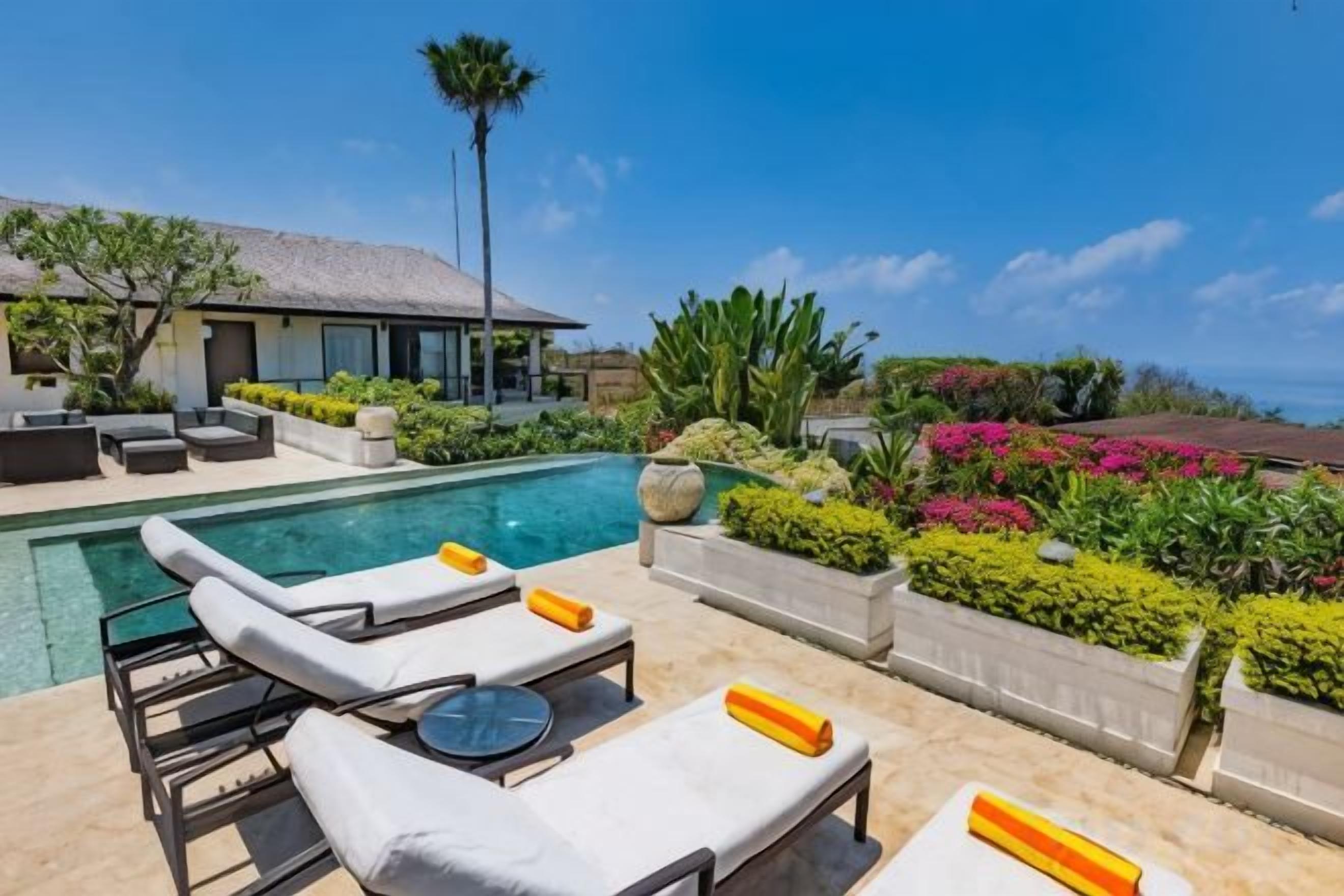 A pool area with lounge chairs and a view of a house.