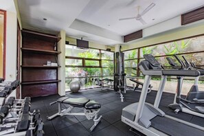 A gym with exercise equipment, a treadmill, and a large window with a view of greenery. - Villa Cantik Pandawa By Fays Hospitality (Bali)
