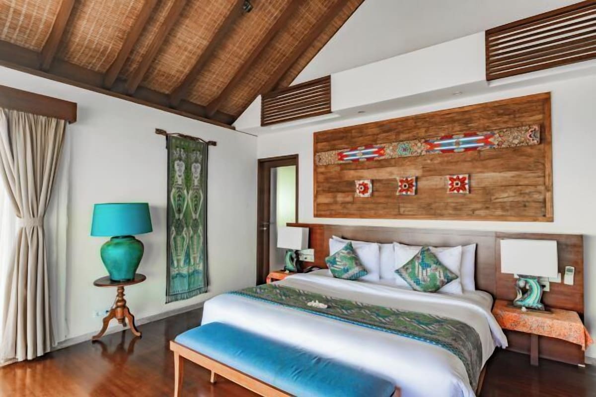 A bedroom with a large bed, wooden headboard, and a decorative wall panel.