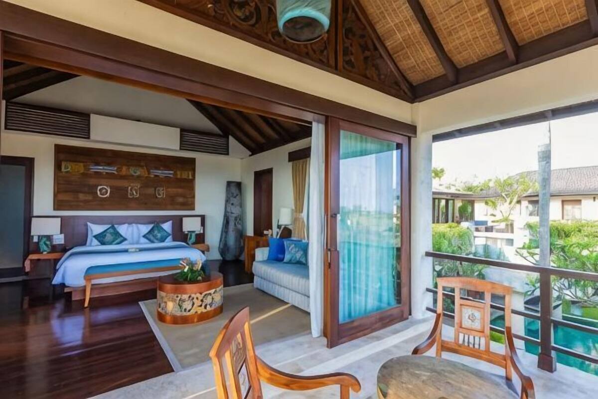 A bedroom with a bed, a sofa, a chair, a table, and a balcony with a view.