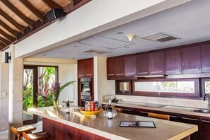 A modern kitchen with a central island, dark wooden cabinets, and a view of greenery outside. - Villa Cantik Pandawa By Fays Hospitality (Bali)