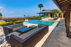 A poolside area with a wicker sofa and a small table, surrounded by a well-maintained garden and a view of the ocean. - Villa Cantik Pandawa By Fays Hospitality (Bali)