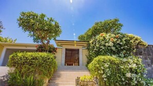 A building with a staircase leading to a door, surrounded by lush greenery and flowering plants. - Villa Cantik Pandawa By Fays Hospitality (Bali)