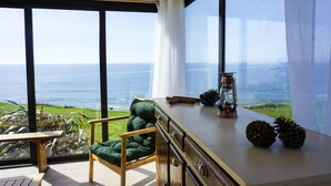 Un balcón con vista al mar, una silla de madera, una mesa y elementos decorativos como un farol y piñas.