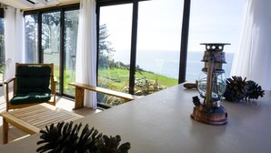 Una habitación con un ventanal grande que da a una vista panorámica, una mesa de madera, una silla verde y una lámpara metálica decorativa.