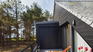 Ein modernes Haus mit dunkler Fassade, einem Balkon mit einem Holzstuhl und einer Reihe von Tulpen.