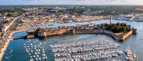 A harbor with numerous boats docked, a fortified structure, and a cityscape in the background.