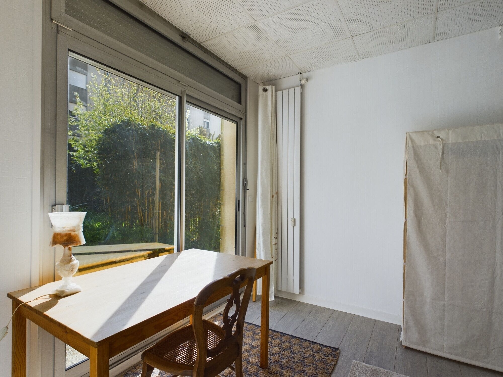 A room with a large window, a table, a chair, and a radiator.