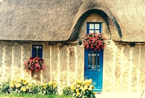 Ein traditionelles Steinhaus mit einem Strohdach, einer blauen Tür und Blumenkörben.