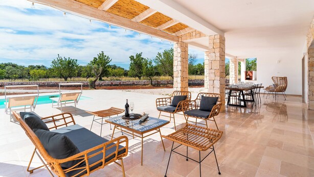 A covered outdoor area with wicker furniture, a pool, and stone pillars.