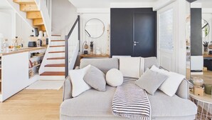 Una sala de estar moderna con un sofá, un plaid a rayas y una escalera que lleva a una cocina.