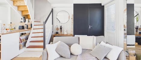 A modern living room with a sofa, a striped throw, and a staircase leading to a kitchen.