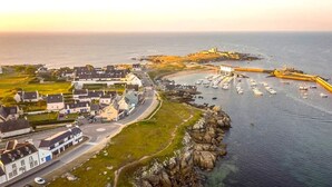 Un pueblo costero con un puerto deportivo, casas y un faro destacado.