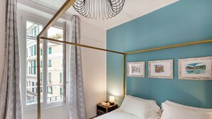 A bedroom with a bed, a nightstand, a lamp, and three framed pictures on the wall. - Art near Lomellini Street by Wonderful Italy (Genoa)