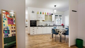 A modern kitchen with white cabinets, a black stove, and a dining area with a table and chairs. - Art near Lomellini Street by Wonderful Italy (Genoa)