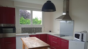 Une cuisine moderne avec des meubles rouges, une table en bois, un four encastré, un four à micro-ondes et une fenêtre donnant sur un paysage verdoyant.
