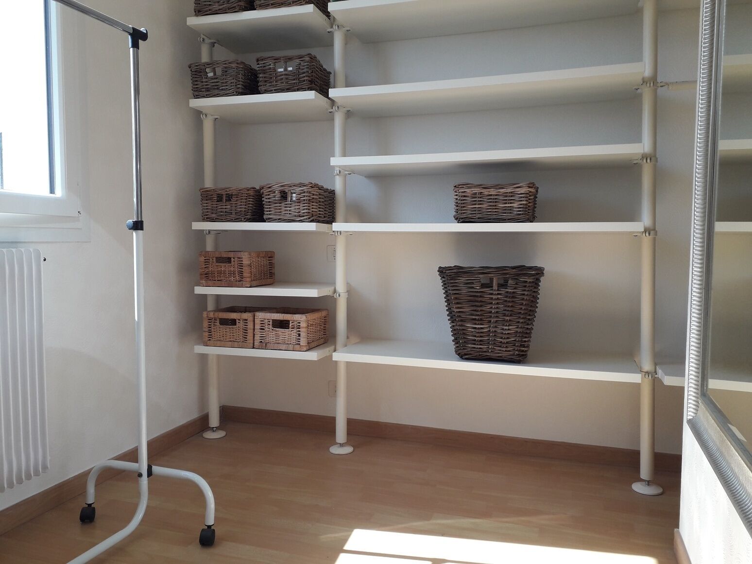 A white metal shelving unit with wicker baskets on shelves.