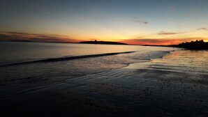 Une plage au coucher du soleil, avec une eau calme et la silhouette d’une côte lointaine.