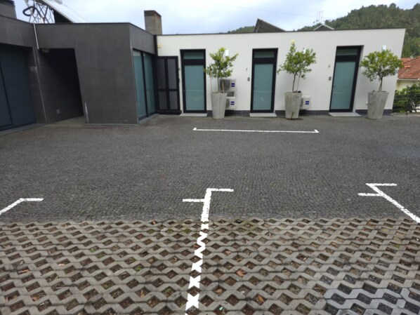 A parking area with marked spaces and a paved walkway leading to a building with multiple doors and potted plants. - Studio superior w/ kitchenett and balcony (Santana)