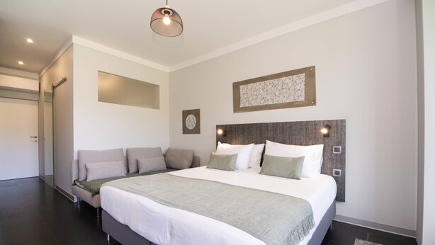 Une chambre moderne avec un grand lit, un canapé, un miroir et une tête de lit dotée d’un éclairage intégré.