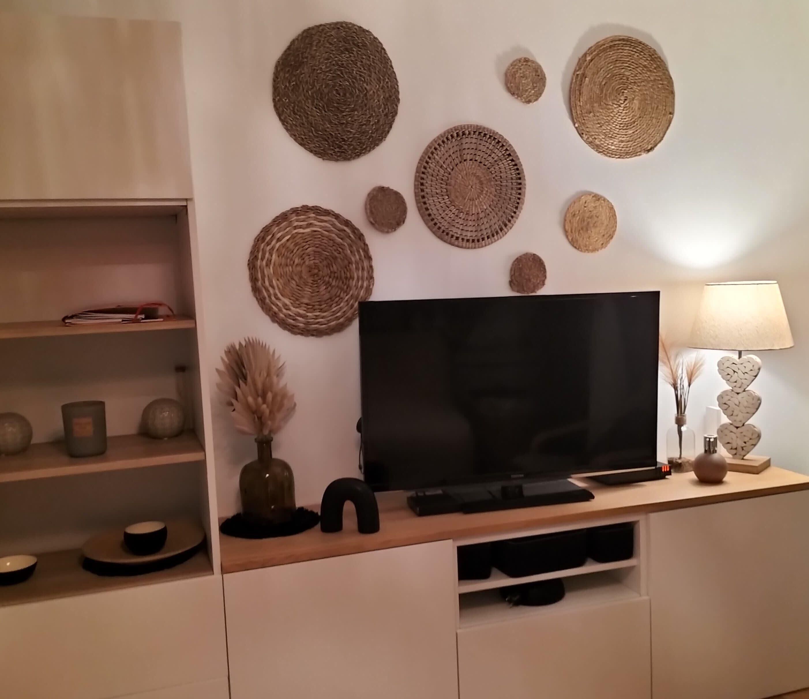 Una sala de estar moderna con un televisor de pantalla plana, estanterías con objetos decorativos y una lámpara con forma de corazón.