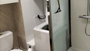 Un baño con inodoro, ducha y zona de ducha con mampara de vidrio.