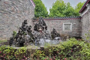 Un patio con una pared de ladrillo tradicional, una fuente de piedra y un techo de tejas.