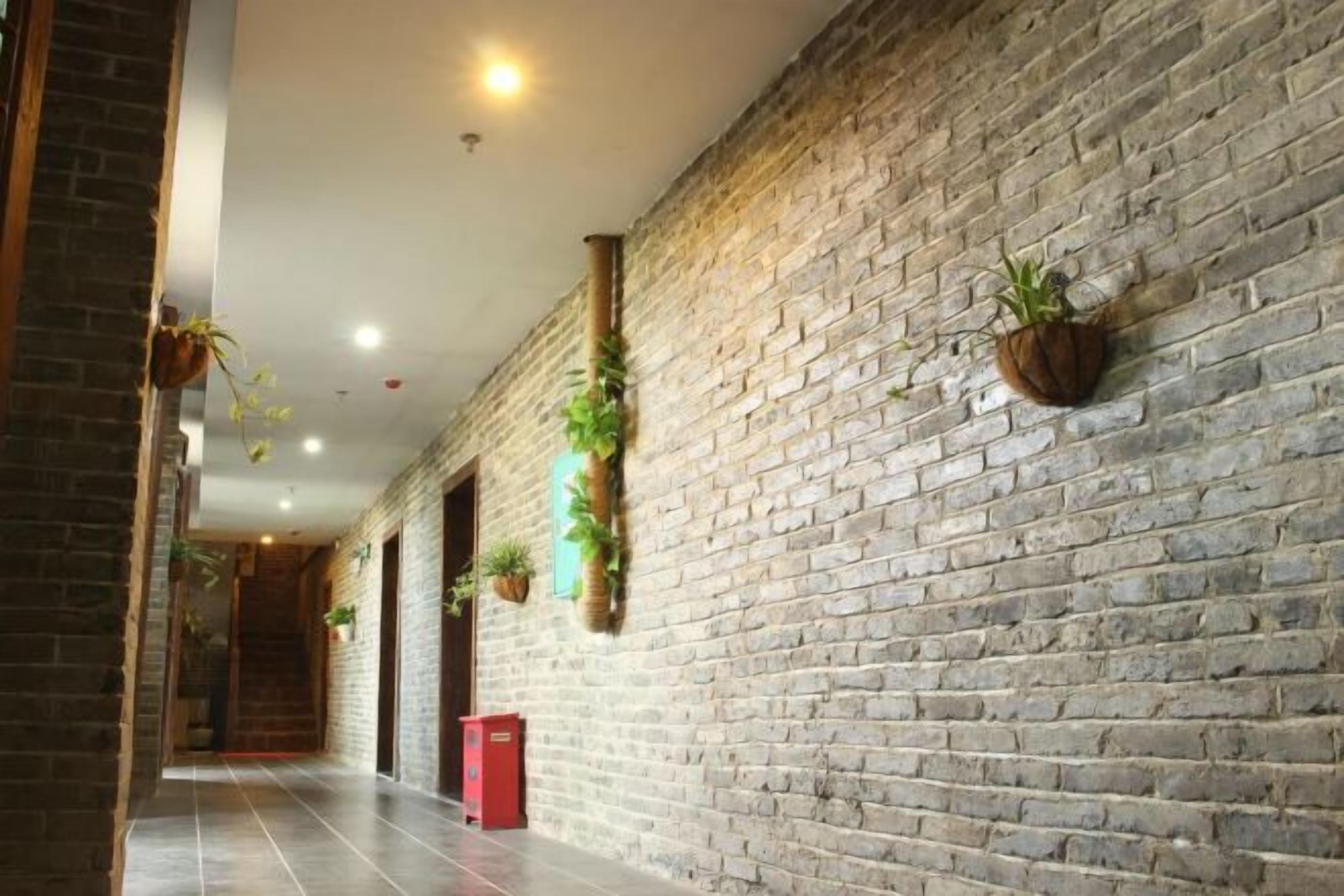 A corridor with brick walls, hanging plants, and a red mailbox.