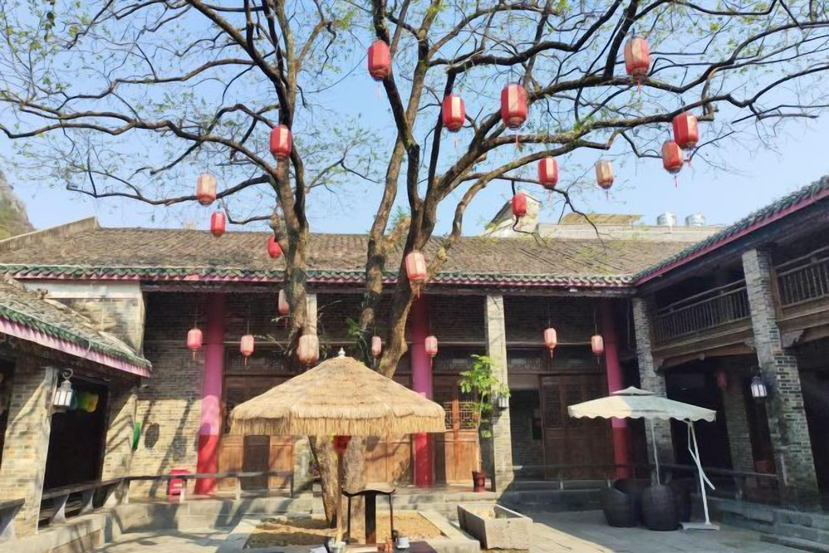 Un patio tradicional con un árbol, faroles y una estructura de techo de paja.