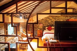 A cozy room with a brick wall, a bed with a red pillow, a TV, and a wooden chair.