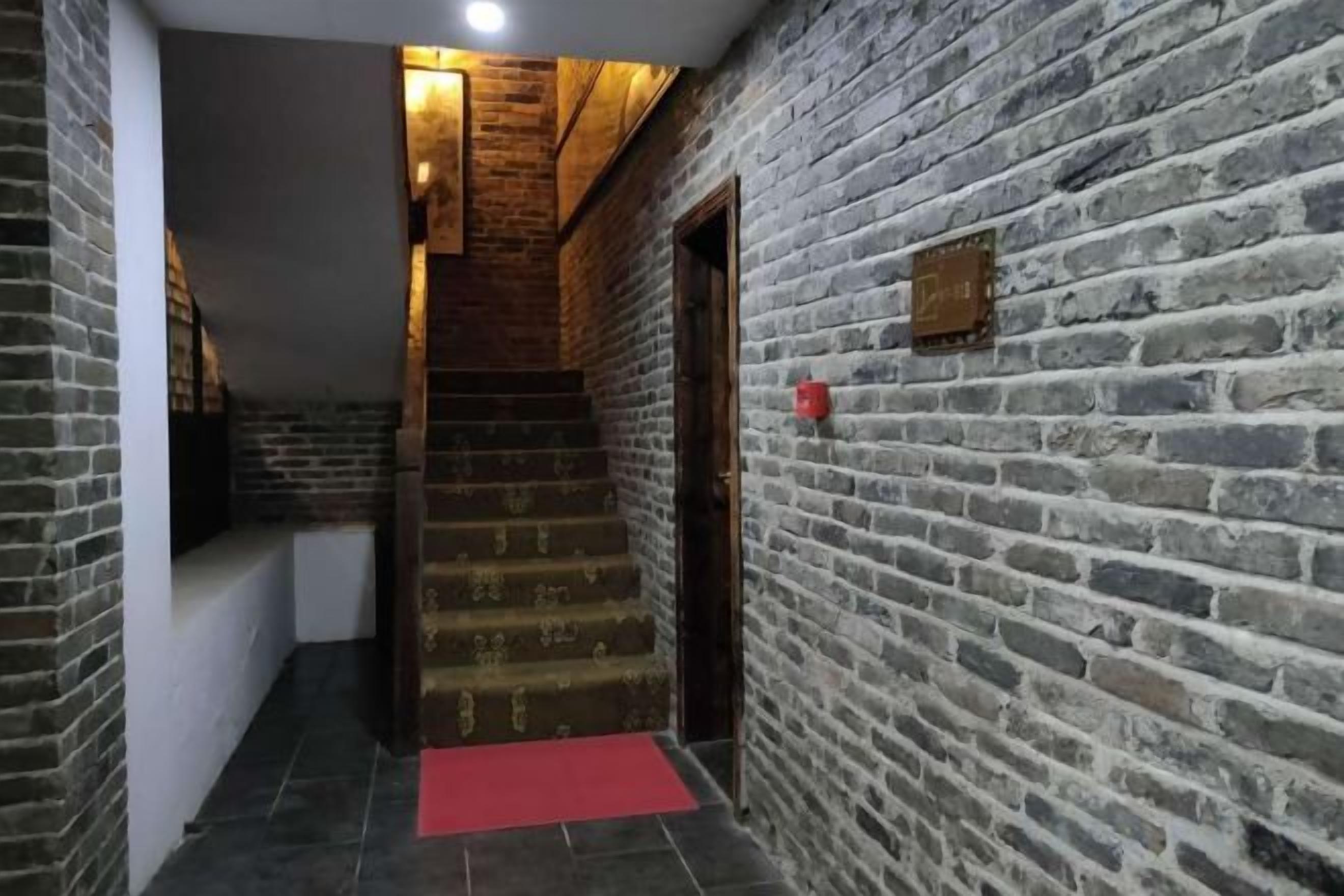 A staircase with a red carpet leading to a door, surrounded by brick walls.