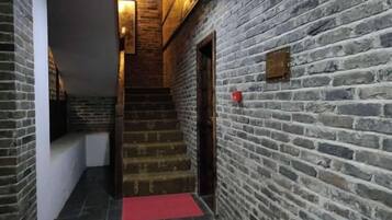 A staircase with a red carpet leading to a door, surrounded by brick walls.