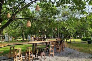 An outdoor dining area with wooden tables and stools, surrounded by trees and hanging lanterns. - Huangyao Bandao Hotel (Zhaoping)