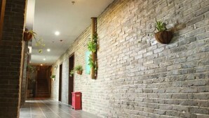 Un couloir avec un mur en briques, des plantes en pot et une poubelle rouge.