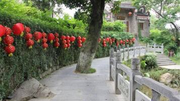 Un sendero flanqueado por faroles rojos, una cerca de piedra y un edificio tradicional al fondo.