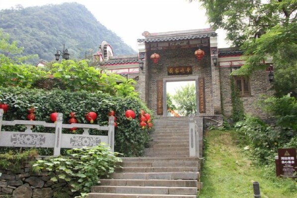 Ein traditionelles chinesisches Tor mit Stufen, umgeben von Grünpflanzen und einer Steinmauer.
