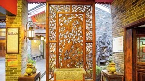 Une cour traditionnelle agrémentée d’un paravent en bois orné de sculptures complexes, d’un banc en pierre et de deux petites tables décorées d’objets d’ornement.