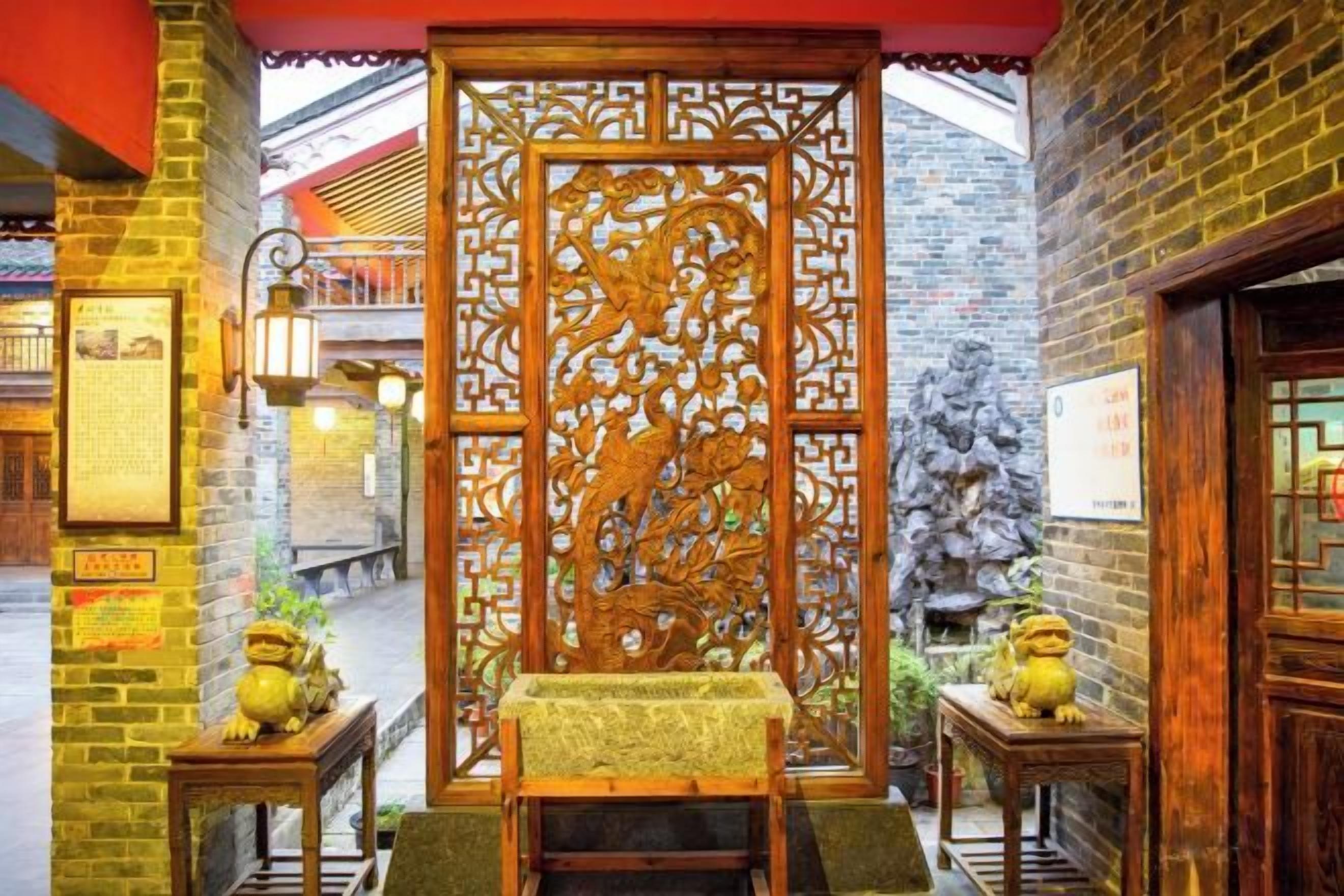 A traditional Chinese courtyard with a wooden screen, a stone lion statue, and a tiled roof.
