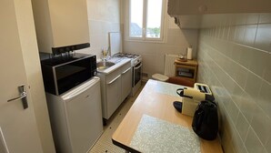 Une cuisine de taille réduite, équipée d’une cuisinière, d’un évier et d’une fenêtre qui laisse entrer la lumière naturelle.