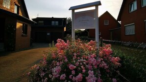 Un bâtiment avec une enseigne, entouré d’un jardin où fleurissent des fleurs roses, et un ciel dégagé.