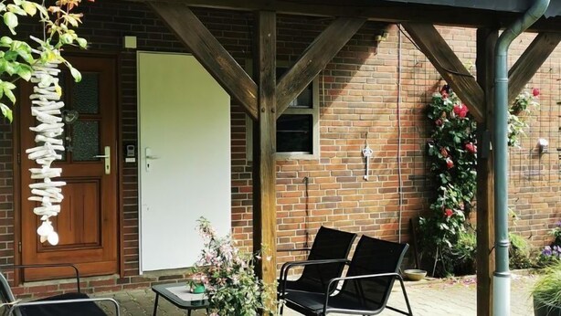 Un bâtiment en briques doté d’un patio couvert, de deux chaises, d’une petite table et d’une plante en pot.