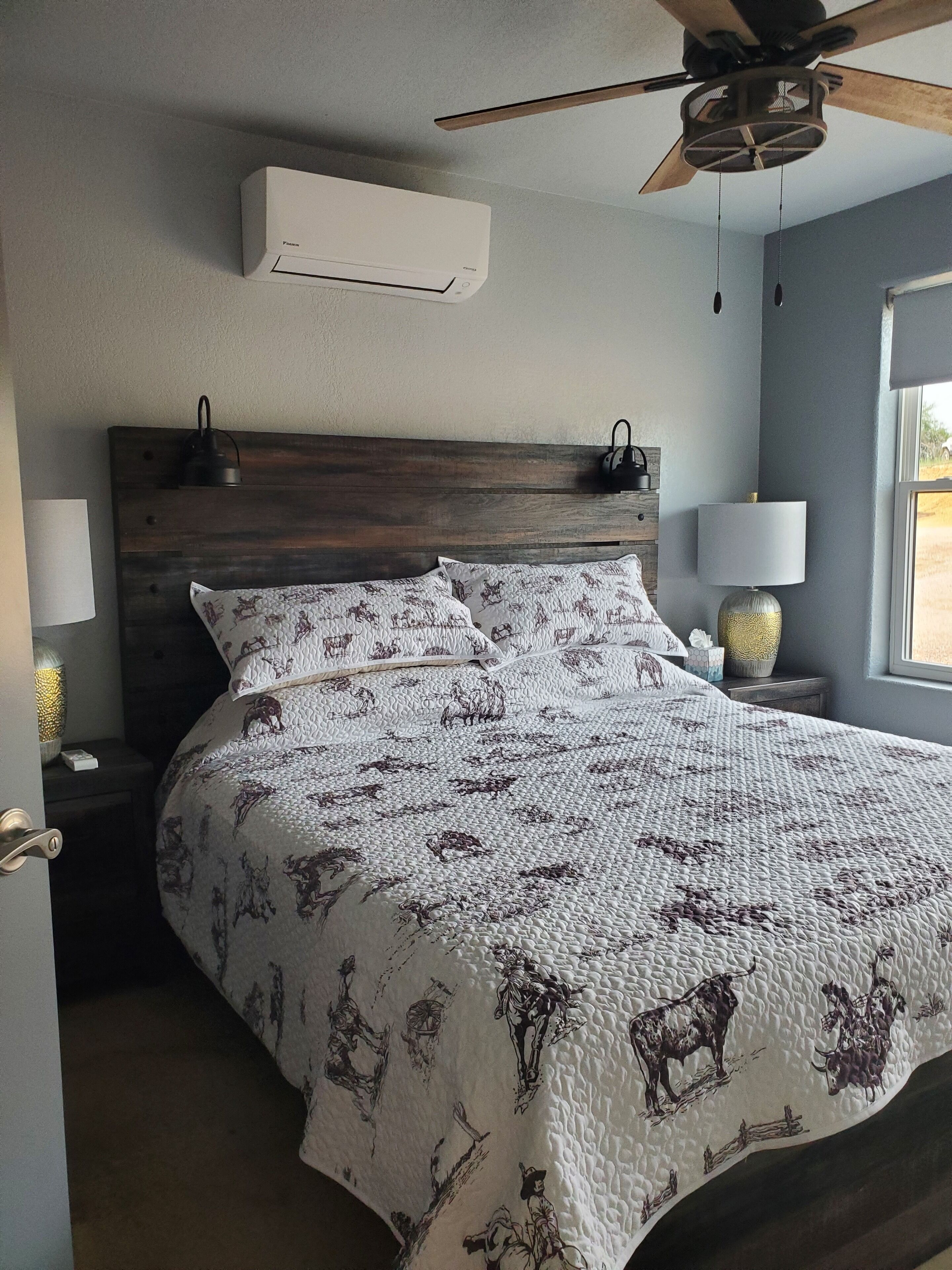 A bedroom with a wooden headboard, a bed with a quilted blanket featuring animal prints, two bedside lamps, and a ceiling fan.